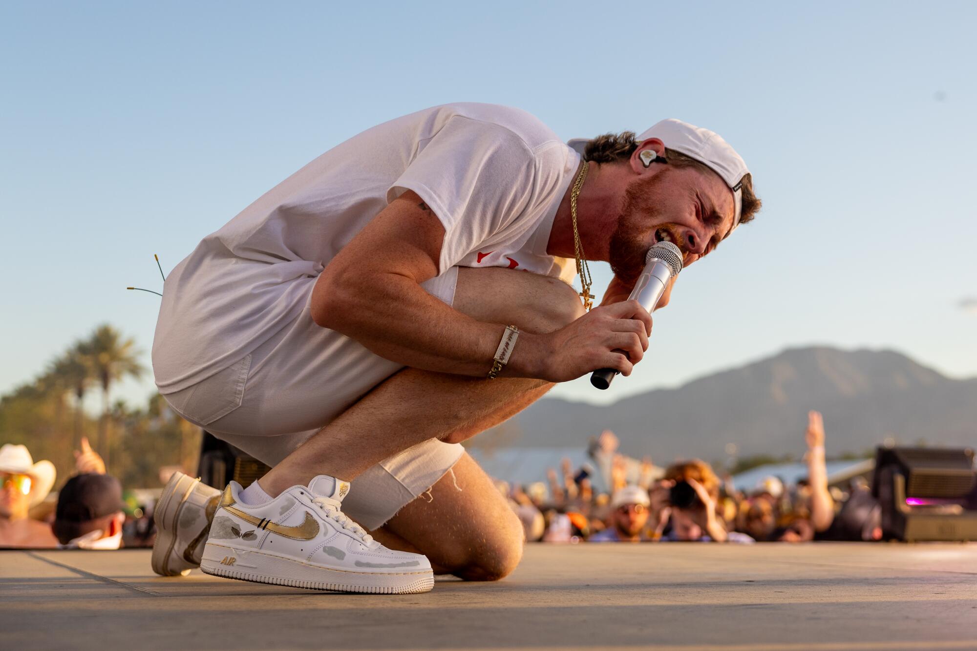 Bailey Zimmerman kneels as he performs on stage at Stagecoach with the mountains in the background
