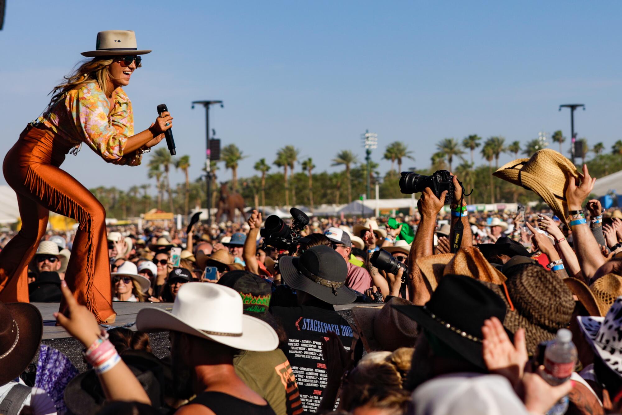 Lainey Wilson performs on the Mane Stage at Stagecoach with a line of palm trees behind her