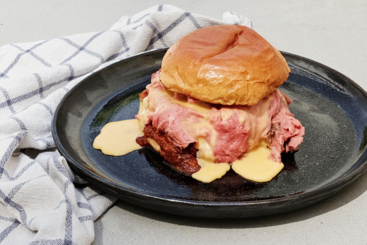 A roast beef sandwich dripping with cheddar sauce on a black plate