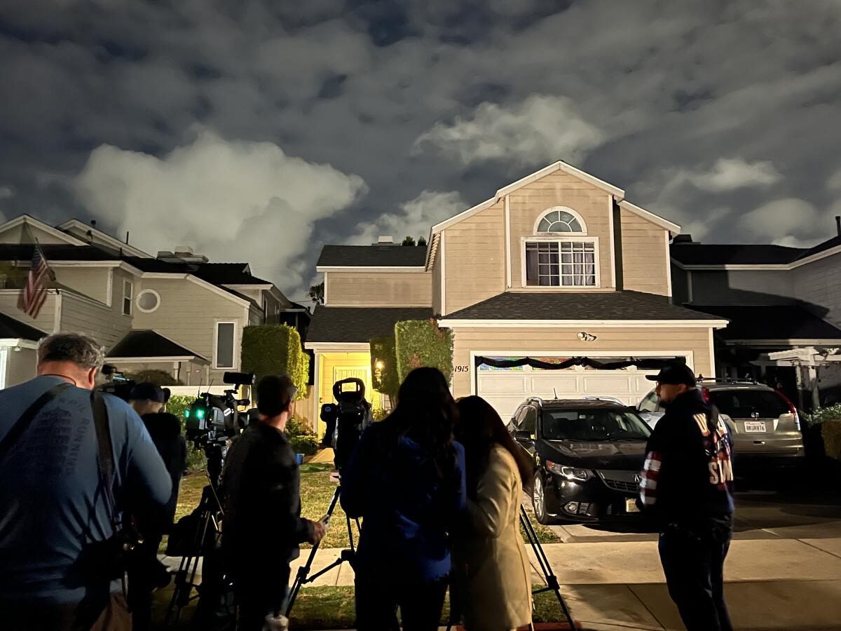 People set up cameras and lights in front of a tan two-story home suburban home.