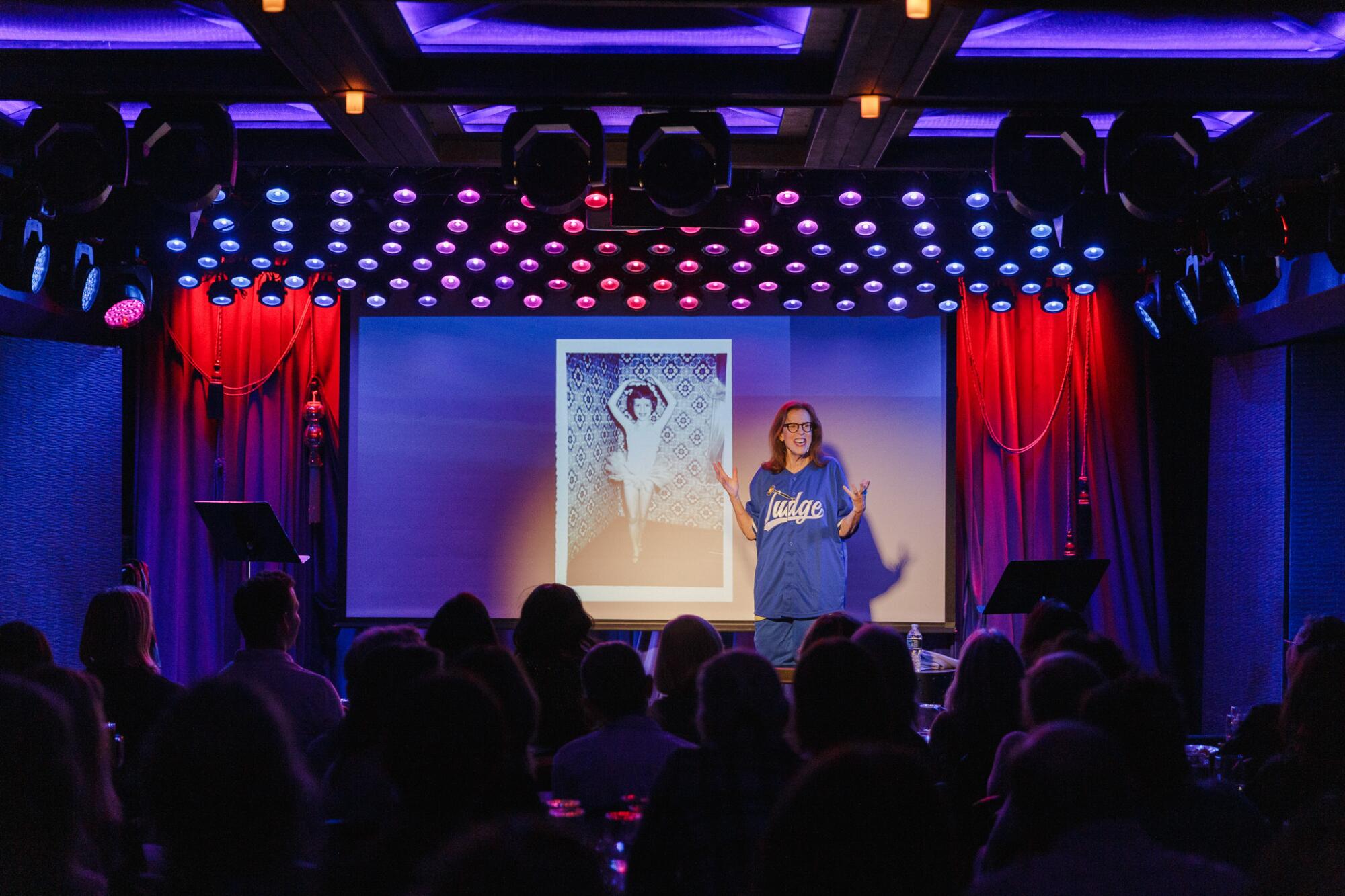 A woman talks on-stage to the audience.