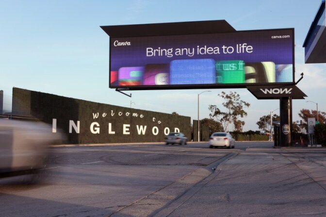 A large digital billboard stretches across a street as cars pass by next to large signage that reads "Welcome to Inglewood."