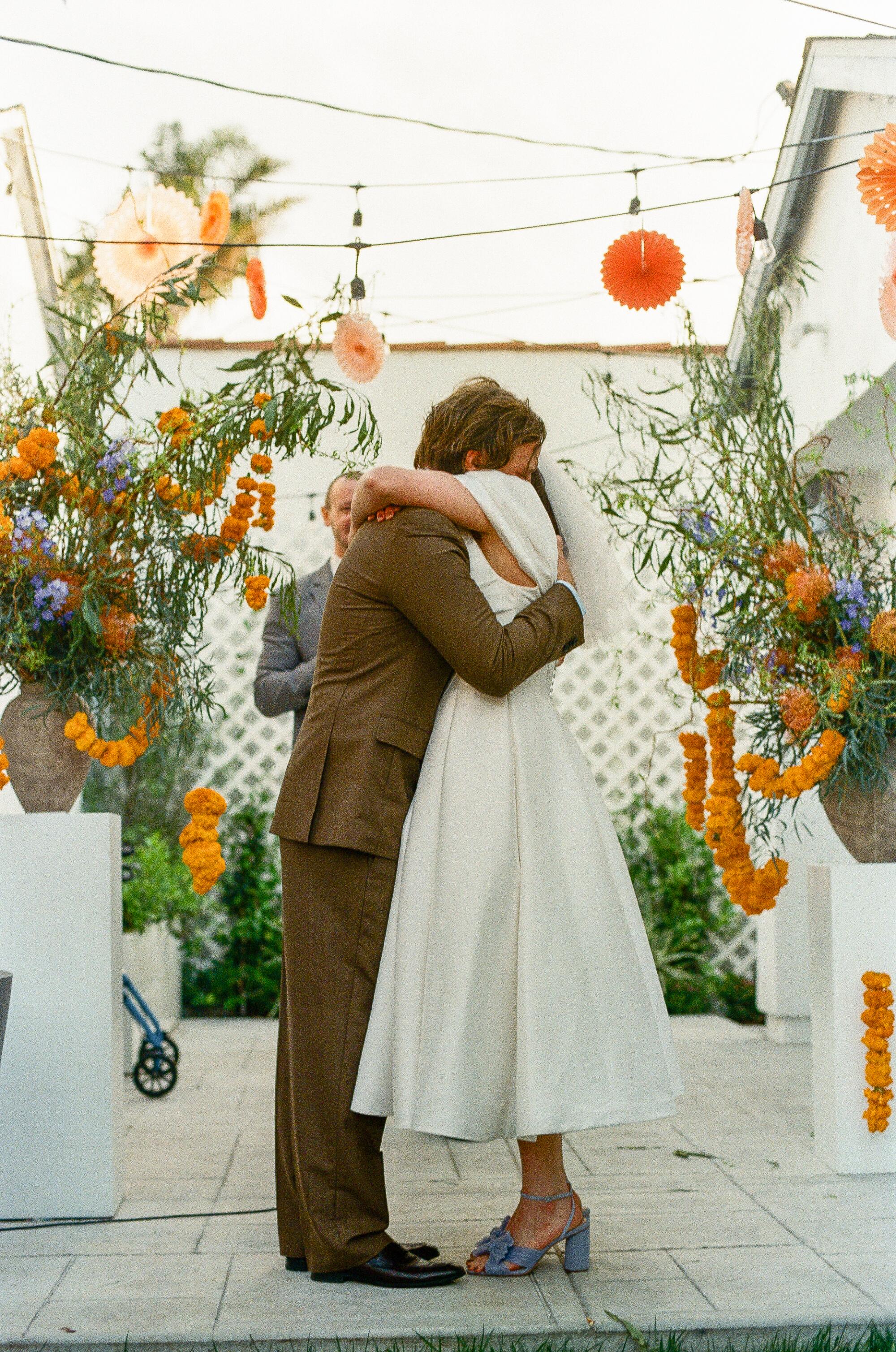 A bride and groom hug on a backyard patio.