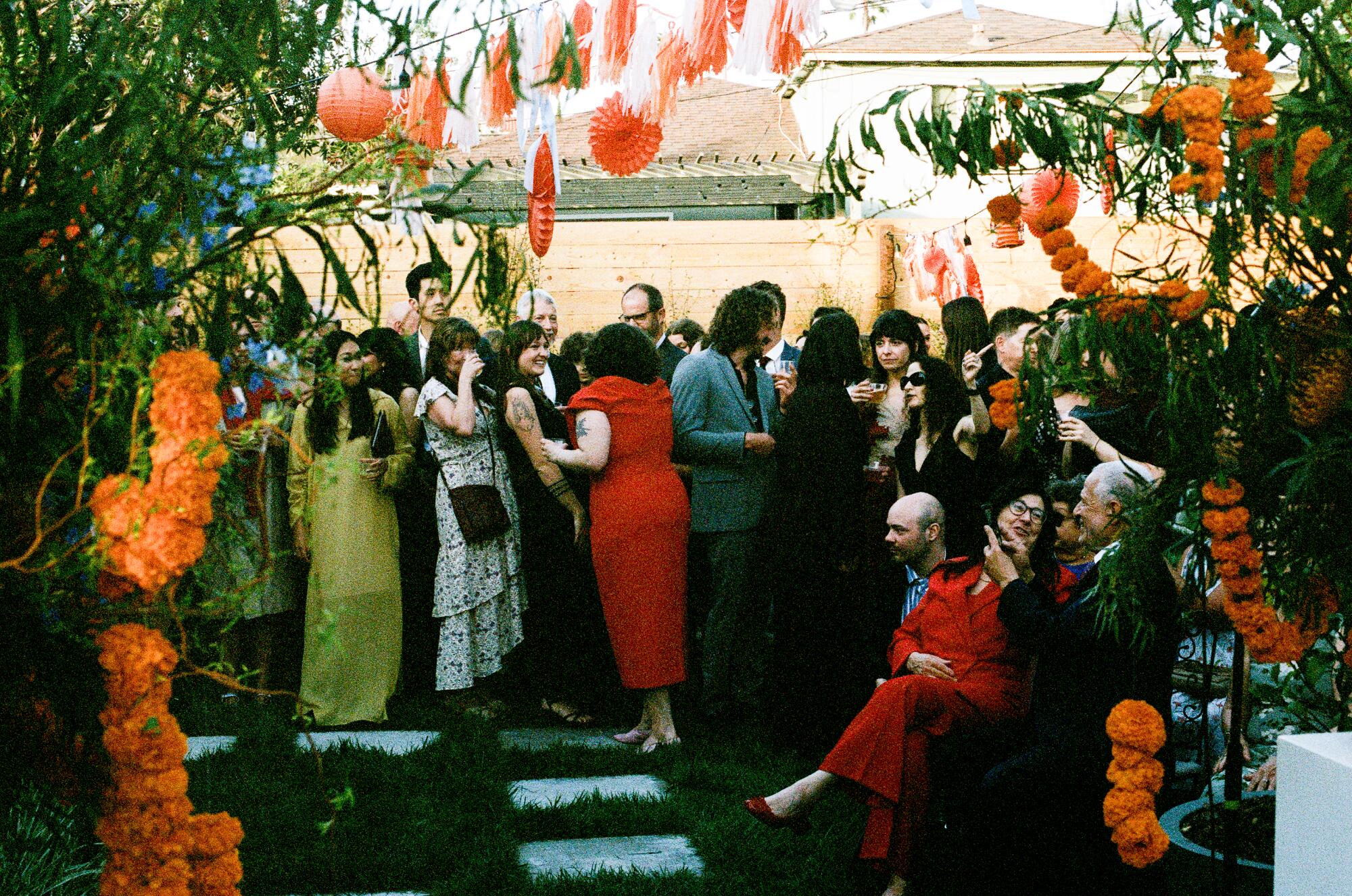 A crowd of people smile and chat in a backyard decorated with marigold garlands. 