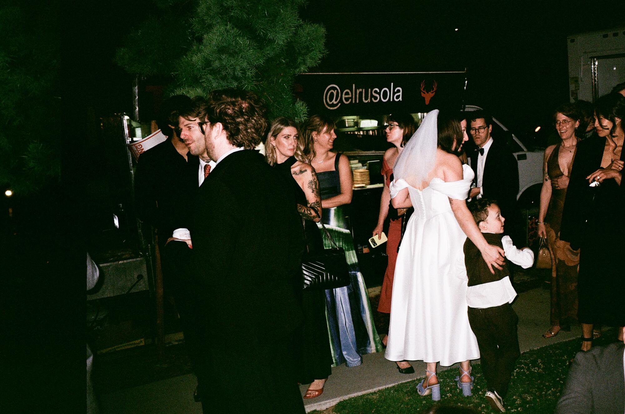 A bride in a veil and tea-length dress mingles with guests near the El Ruso taco truck.