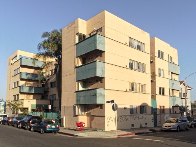 A dilapidated apartment building painted pink and green, with graffitied walls and broken windows, is seen in Hollywood.