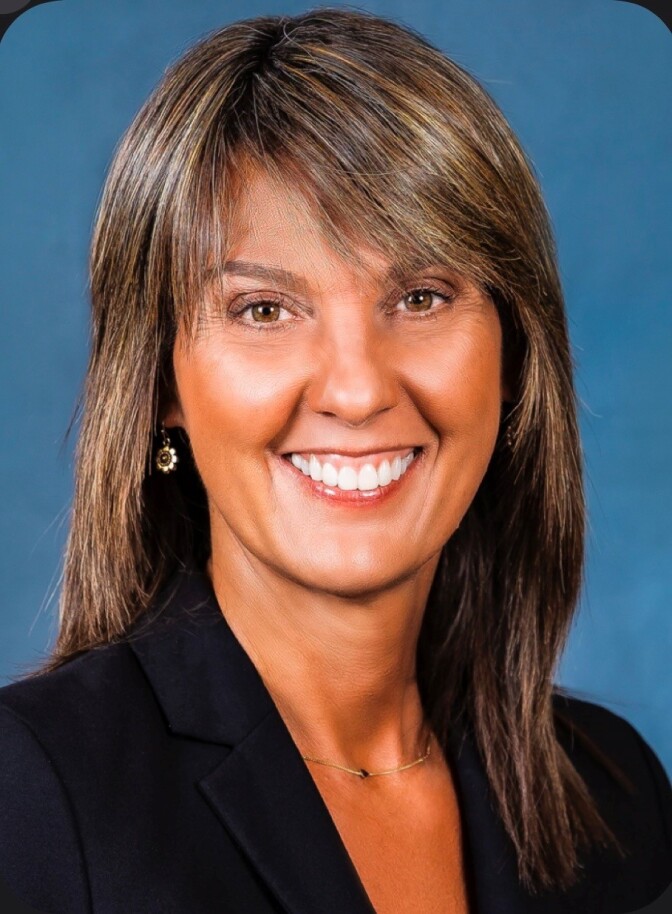 a smiling woman with shoulder-length brown hair wearing a black blazer