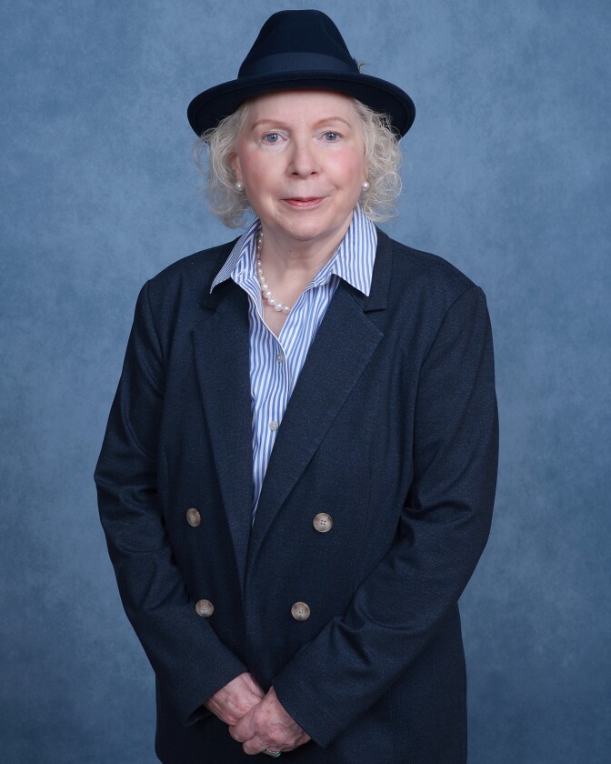 An older white woman wears a blue suit and a hat.
