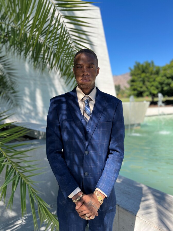 a man in a dark blue checkered suit with a checkered tie stands in front of a fountain