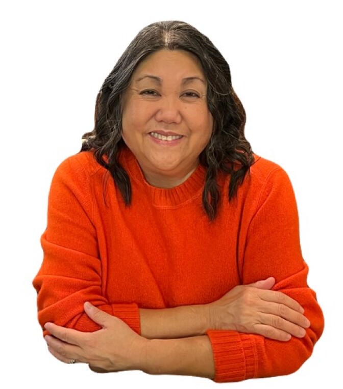 A woman with medium skin tone and dark hair crosses her arms while wearing a red sweater.