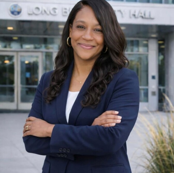 A woman with medium-dark skin tone and dark hair crosses her arms. She wears a blue blazer.