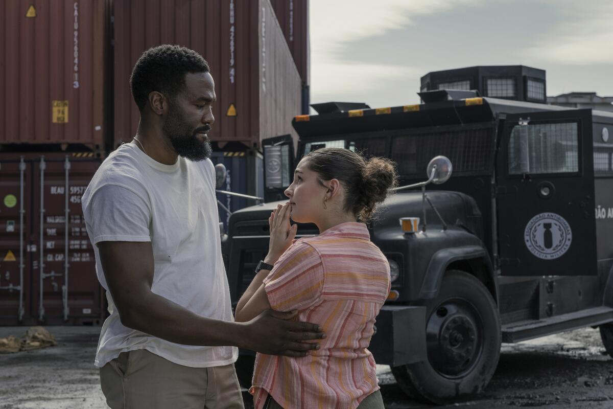 A man in a white T-shirt looks down at a teenage girl standing in a storage yard.