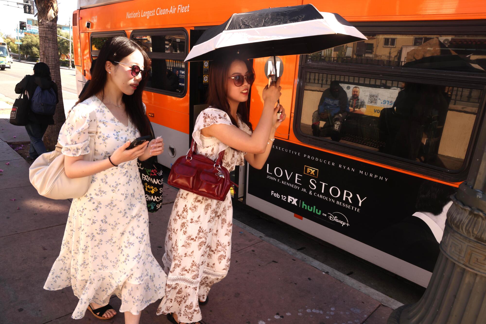 A pair of visitors from Japan rush to catch a Metro bus, one of them under the shield of an umbrella.
