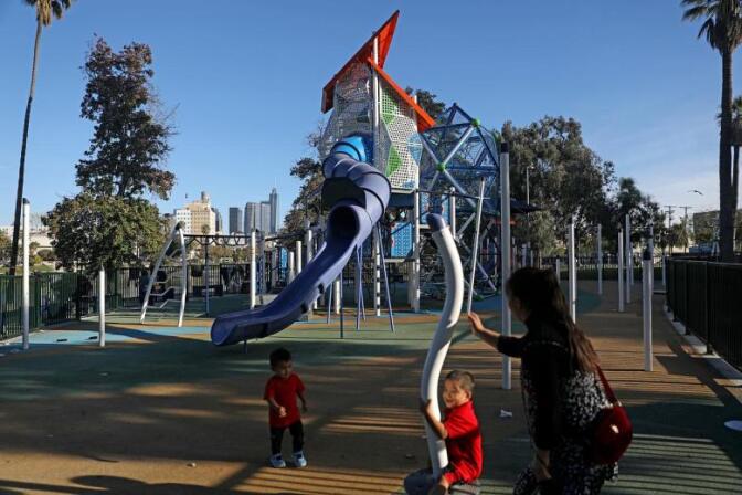 Two children play on a playground apparatus. A woman stands by, watching them.