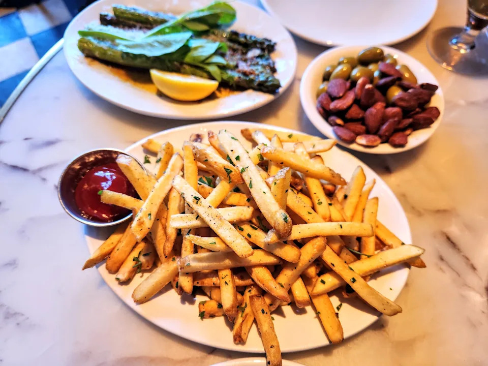 A plate of fries topped with herbs next to a bowl of olives from Bar Sinizki.