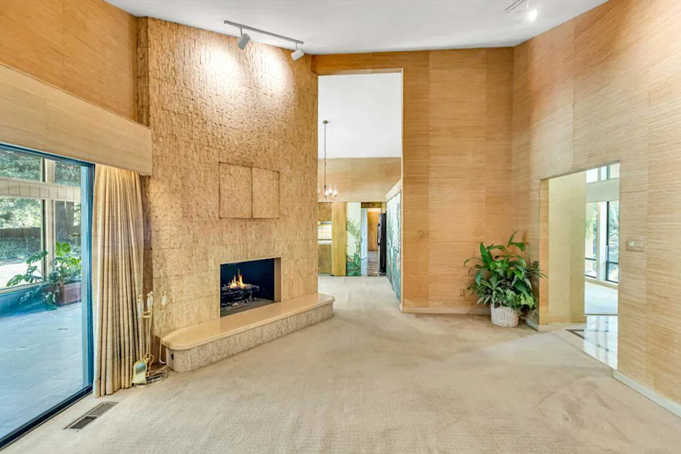 Original grass cloth wallpaper and a travertine stone fireplace preserve the home’s 1970s design aesthetic in pristine condition.