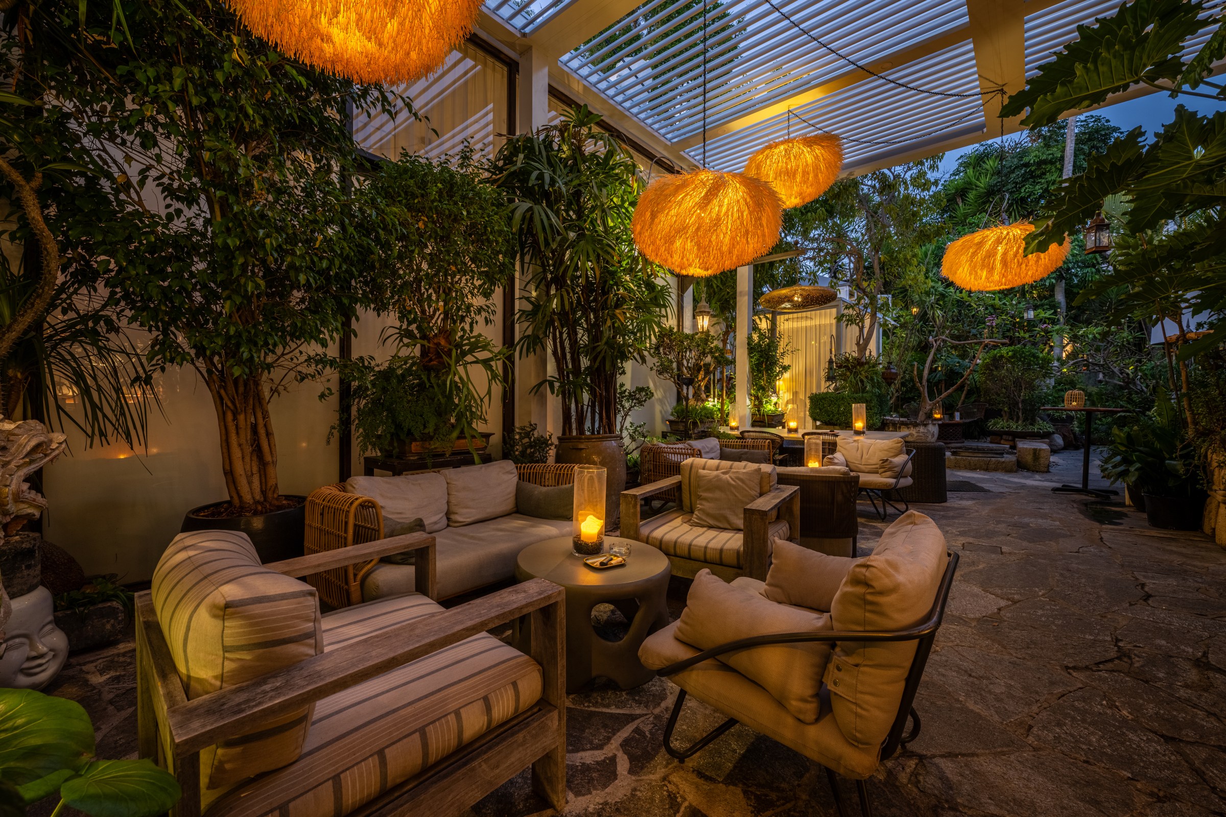 Cushioned chairs and loveseats surrounded by leafy plants and hanging lights at the Woods cannabis lounge in West Hollywood, California.