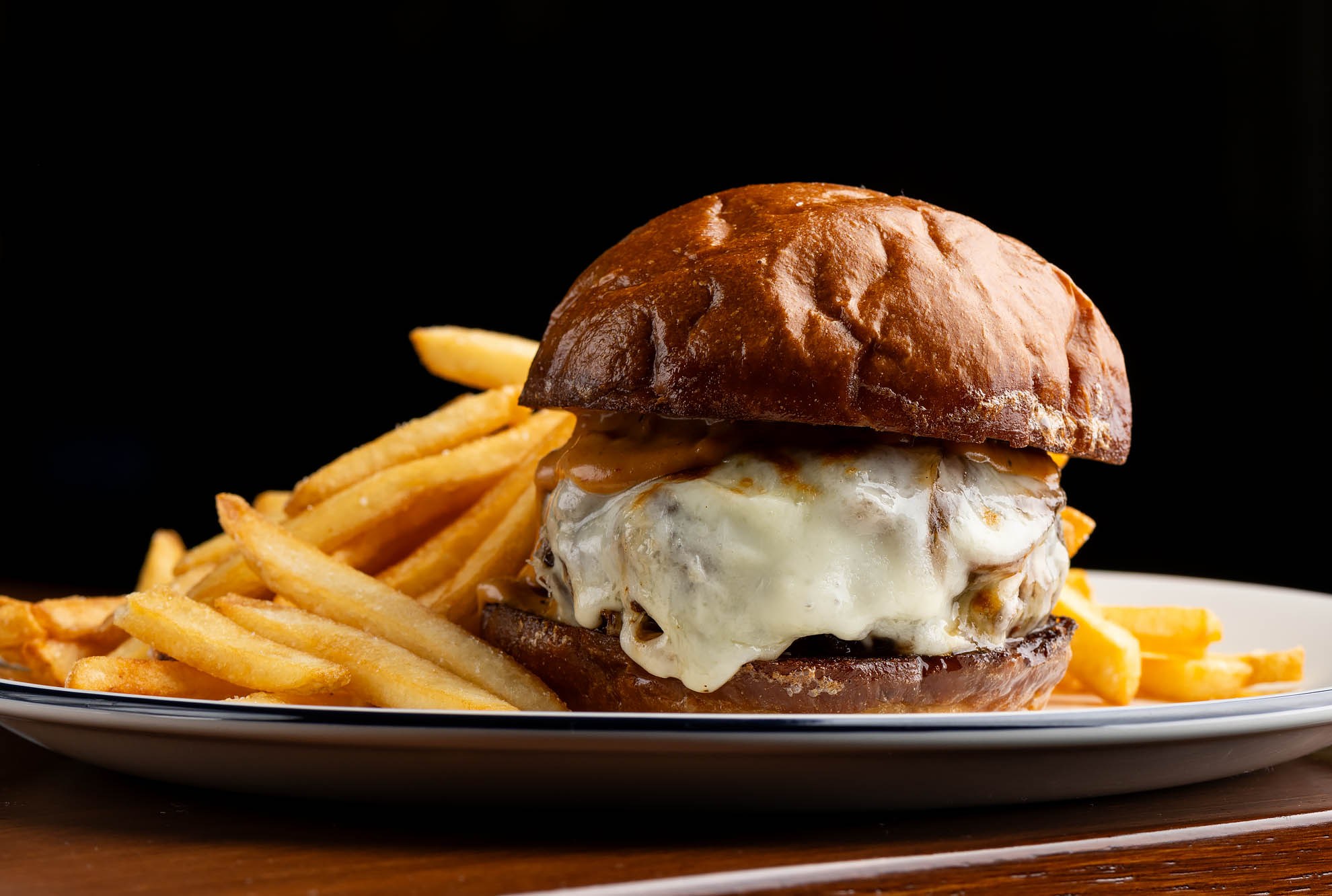 Dry-aged burger with provolone, grilled onions, pickled jalapenos, and French fries at Camelia