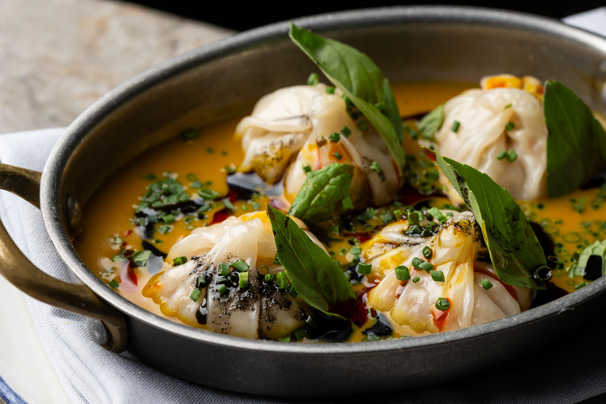 Carefully pleated Afro Caribbean shrimp dumplings served in an orange broth with leafy garnish at Si Mon.