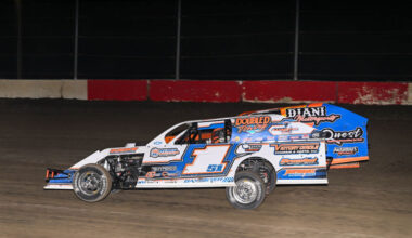 Dirt track race car number 1 on a nighttime race, blue and white livery with sponsor decals.