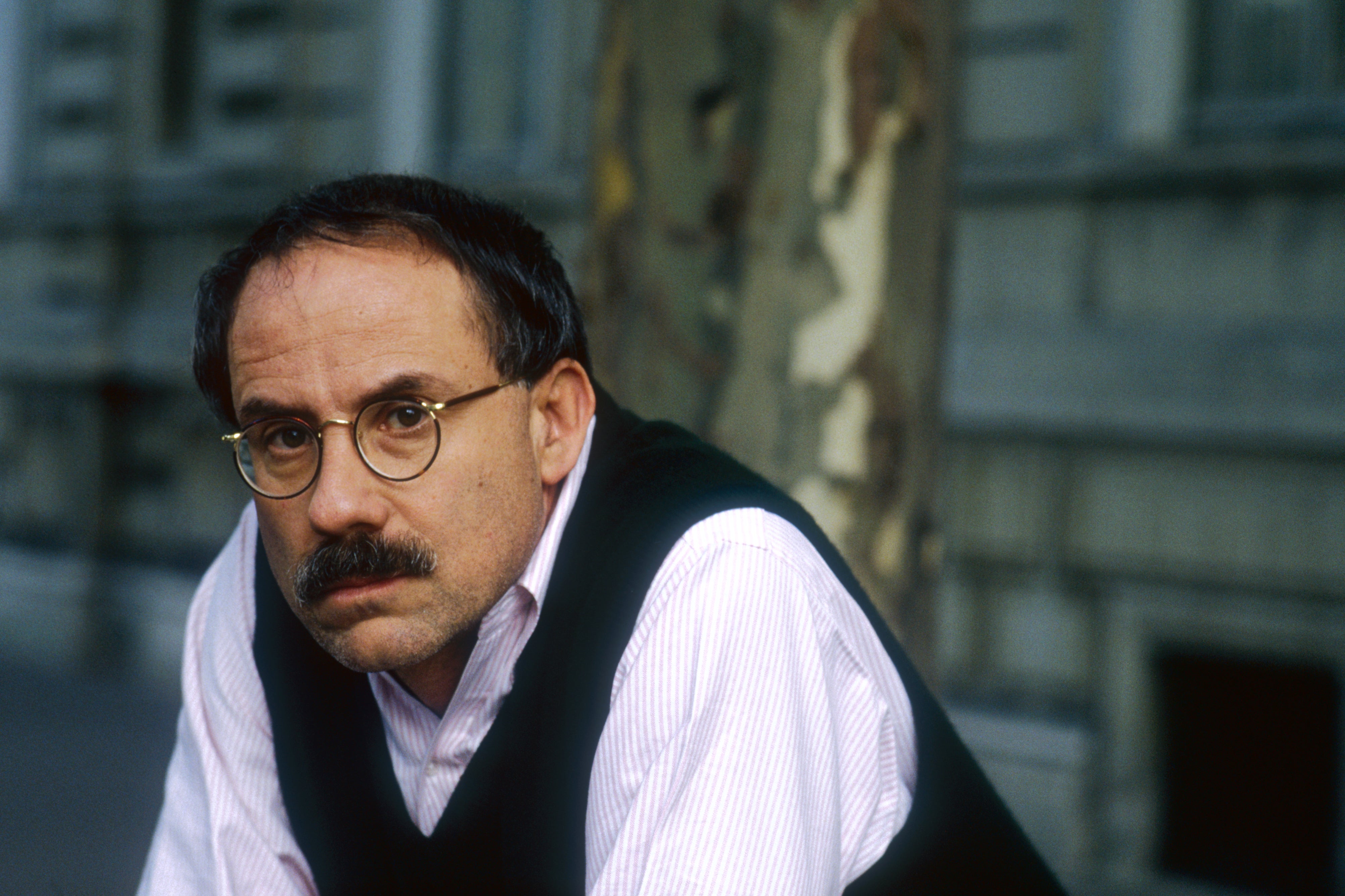 A middle-aged white man with dark hair, a mustache, and wire-rimmed glasses looking pensive.