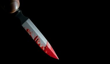 An extreme close-up photograph of a bloodied pocket knife, the harsh flash illuminating the gritty, textured metal surface against a pitch-black background, conceptually representing the violence that erupted at the Fresno ArtHop event.