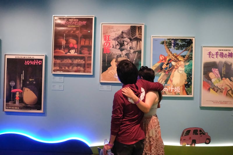 Two visitors pause to view a wall of original Studio Ghibli film posters.