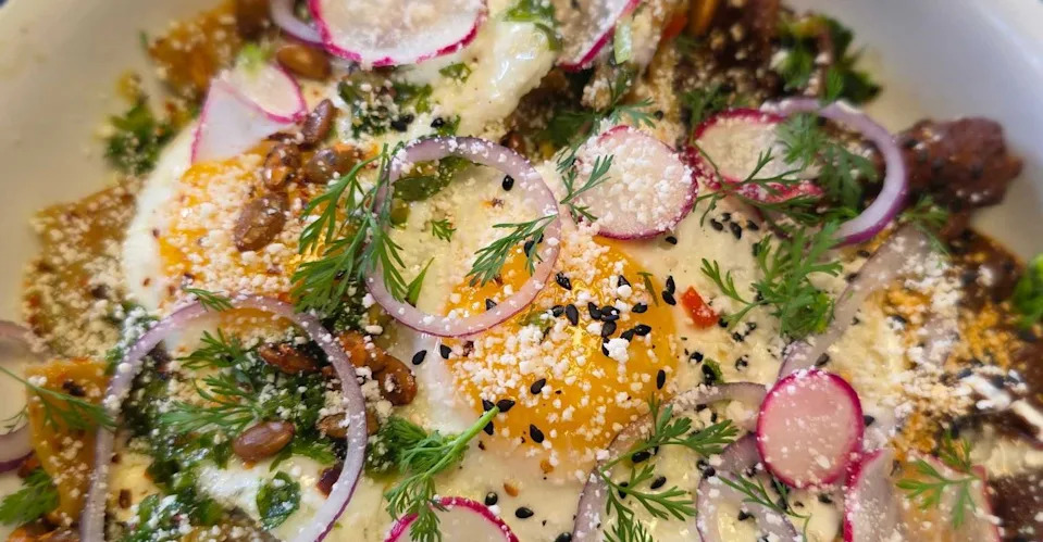 A bowl of chilaquiles topped with thinly sliced radish and a fried egg with green onions from Tenampal.