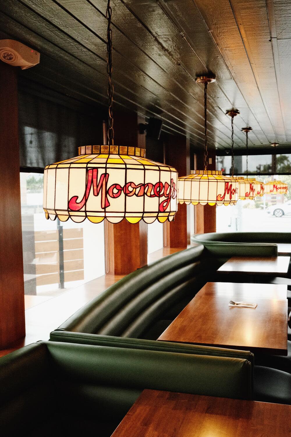 The dining room of Mooney's Pizza Tavern featuring green leather booths, warm wood, and custom stained-glass lanterns.
