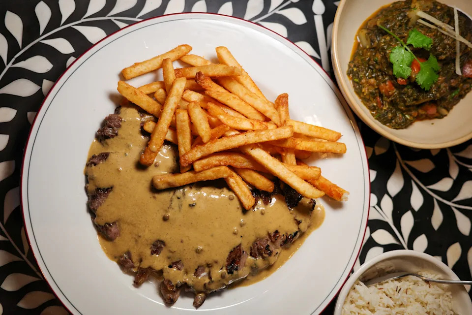A plate of steak frites topped with a masala au poivre sauce with a side dish of chutney.