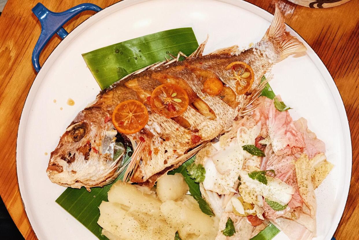 A fried whole snapper with yuca and salad in a large white-and-blue serving tray