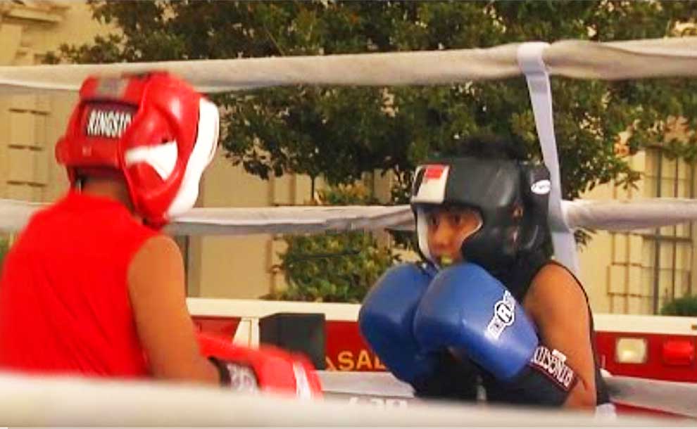 2 kids one wearing red and another wearing blue boxing each other