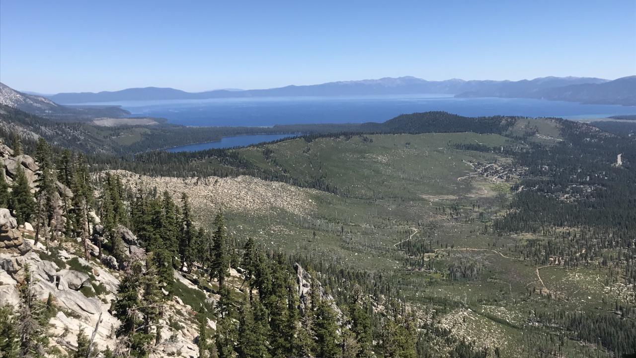 View from rocky slope over pine forests to a blue Lake Tahoe and distant peaks