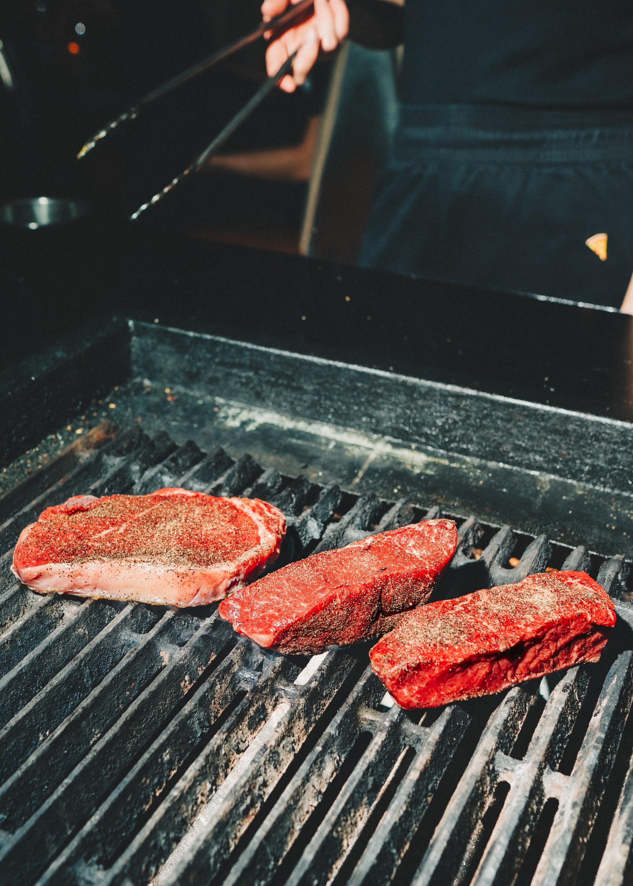 Three seasoned steaks on a grill.