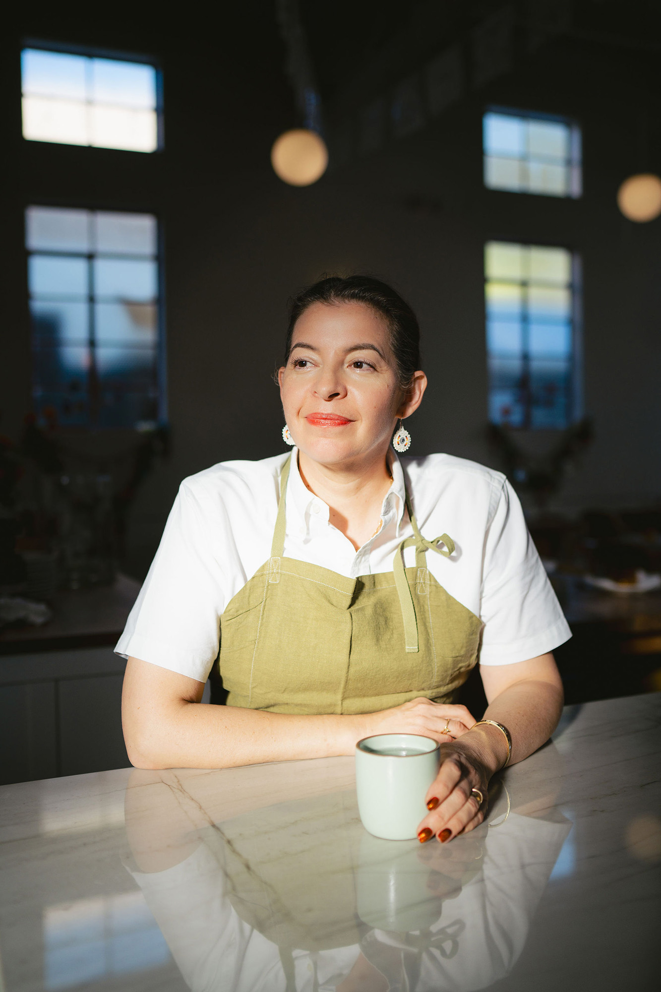 Portrait of a chef in an khaki apron seated at the counter inside a restaurant.