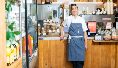 A powdered sugar-dusted croissant with orange zest sits on a white plate, next to an éclair topped with cream and orange slices on another white plate.