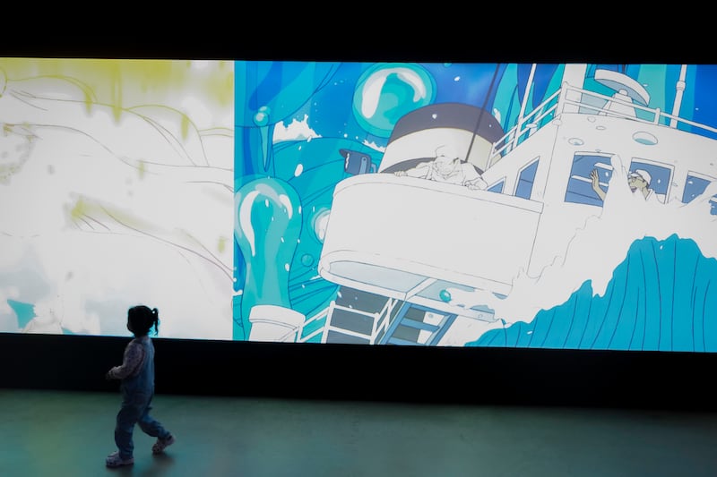 A child crosses the gallery as scenes from Ponyo play across the large screen.