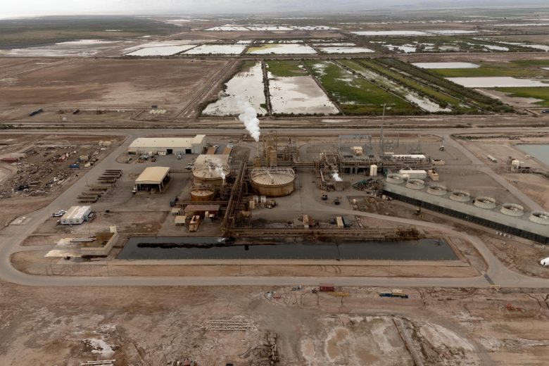 Aerial view of an industrial facility with large tanks and steam, set in a barren landscape with surrounding fields.
