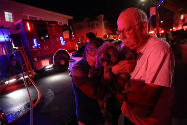 Rory Bannatyne and his wife Terri Coleman hold their dog Bunty and cat Tubbs as Oakland firefighters respond to a two-alarm fire in a large apartment building at 200 Fairmount Avenue in Oakland, Calif., on Tuesday, April 7, 2026. They live in an apartment above the fire and could not find their two other cats to get them out. (Jane Tyska/Bay Area News Group)