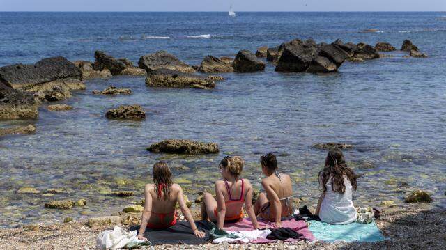 Four young women in swimsuits look at the Mediterranean Sea on the beach of Cala Rossa in Syracuse, Sicily, Italy