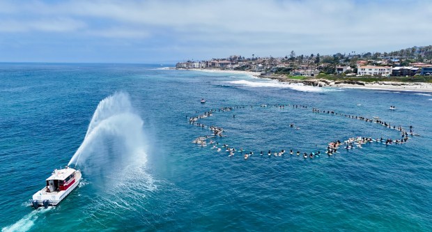 Surfers accompanied by a lifeguard boat pay tribute to late surfer Mike Hynson during a paddle-out at La Jolla's Windansea Beach on June 28. (Santiago Aguerre)