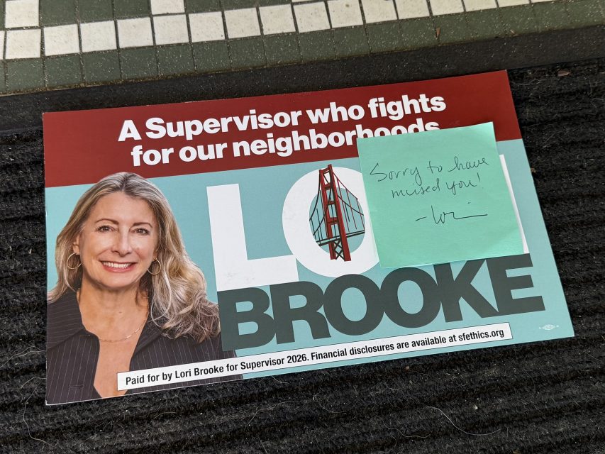 Campaign flyer for Lori Brooke for Supervisor with a handwritten sticky note on top reading, "Sorry to have missed you!" placed on a doormat.