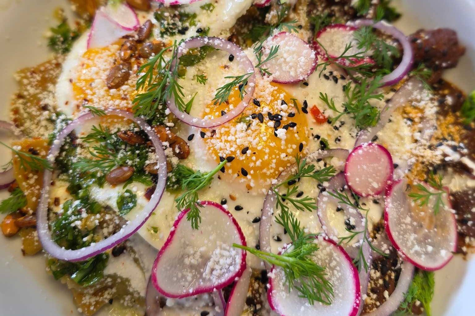 A bowl of chilaquiles topped with thinly sliced radish and a fried egg with green onions from Tenampal.