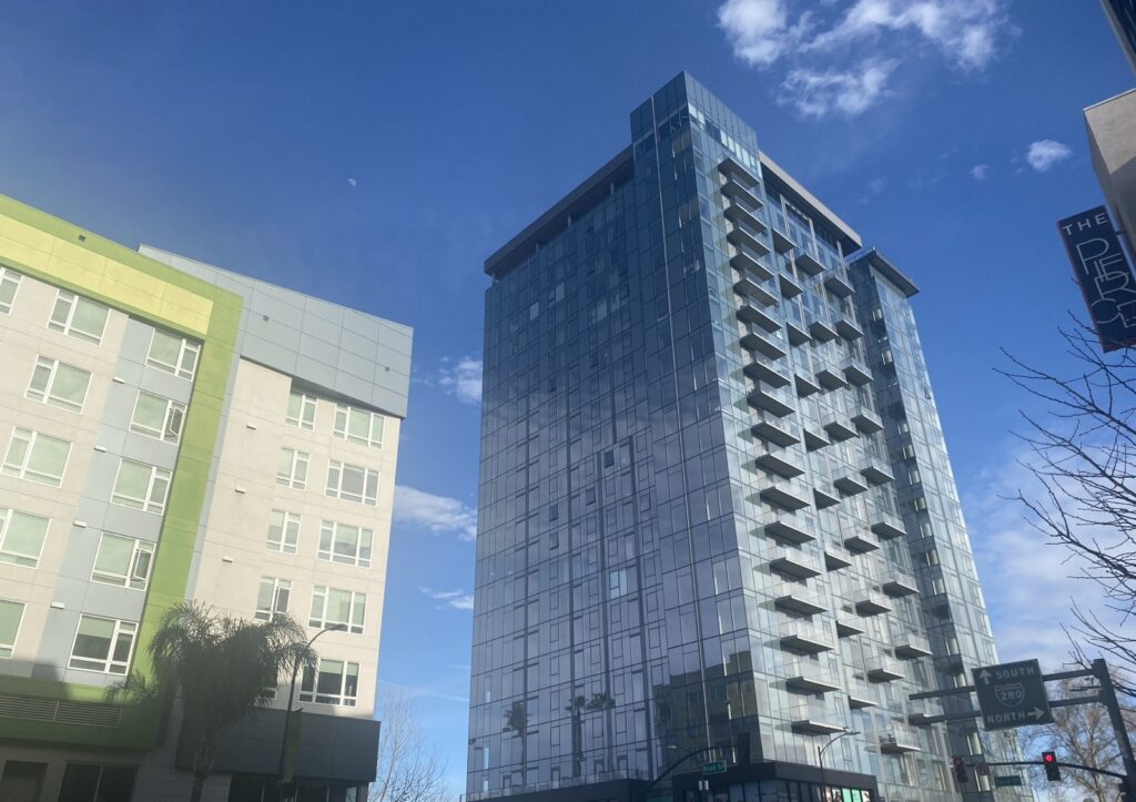 A glass high rise raises up into the sky across the street from a mid-rise apartment.