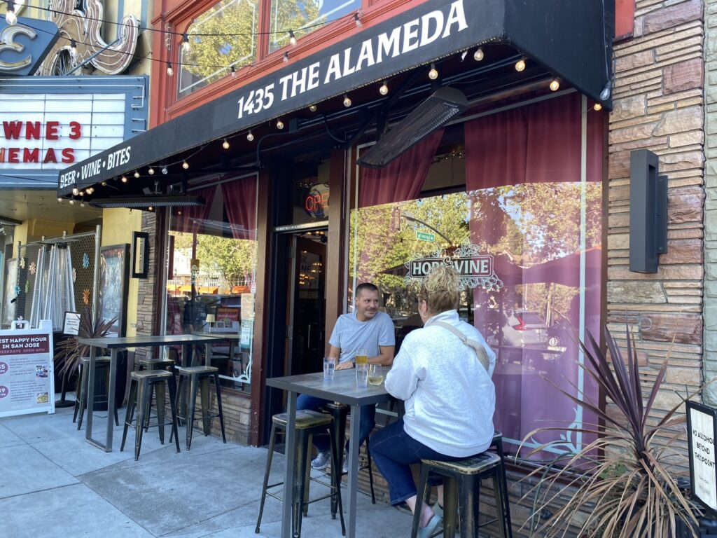 Two bargoers chat in front of a bar.