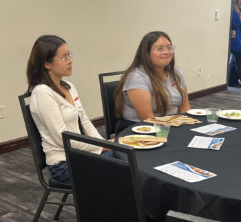 2 students listening to speaker at the front of the room