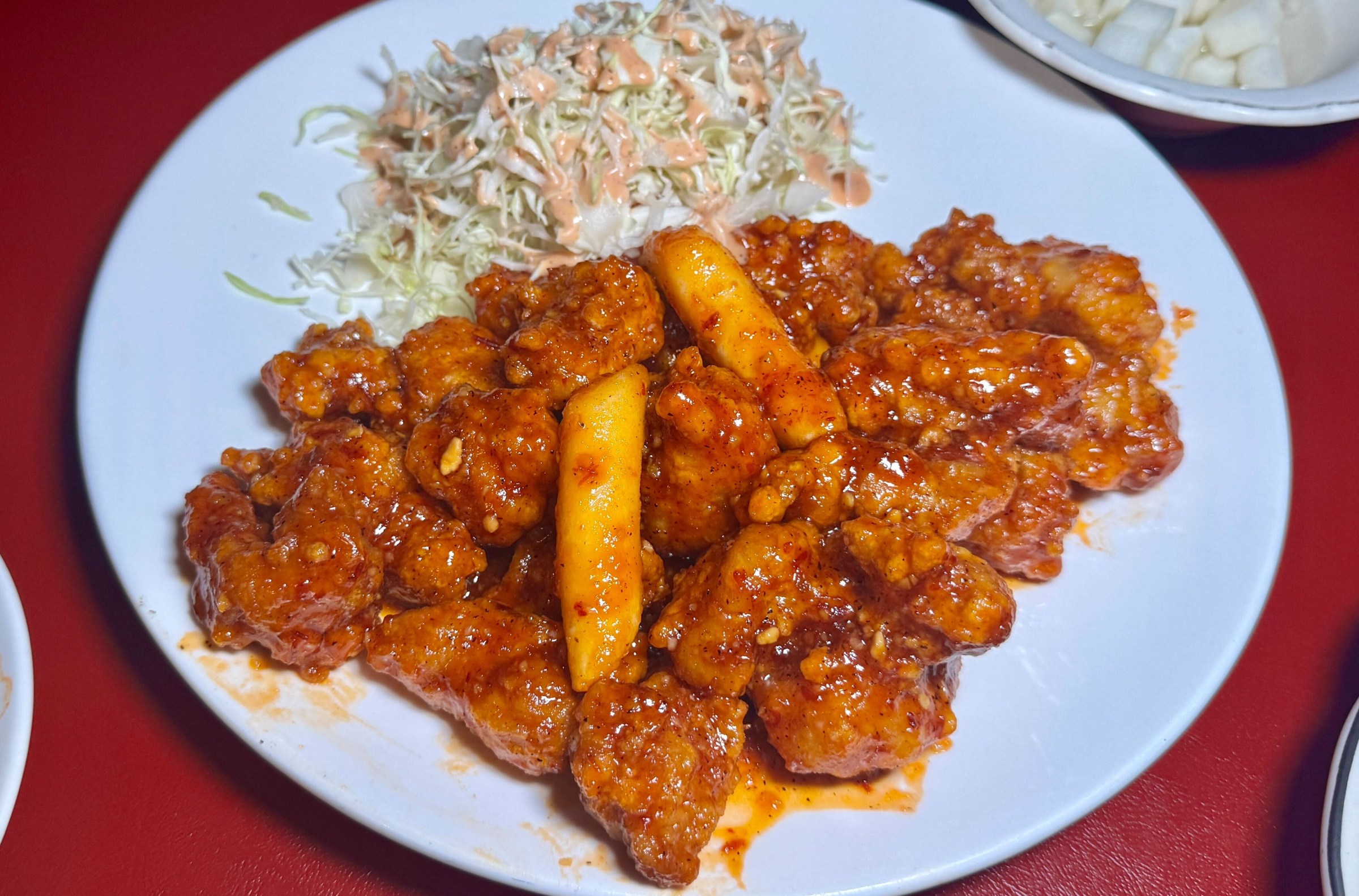 Plate of boneless fried chicken covered in a sweet and spicy glaze with rice cakes and a side of cabbage salad.