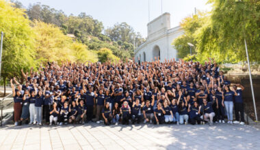 Group portrait of about 300 MBA students posing on steps to the Cal Memorial Stadium. They are wearing Berkeley Haas t-shirts and waving to the camera.