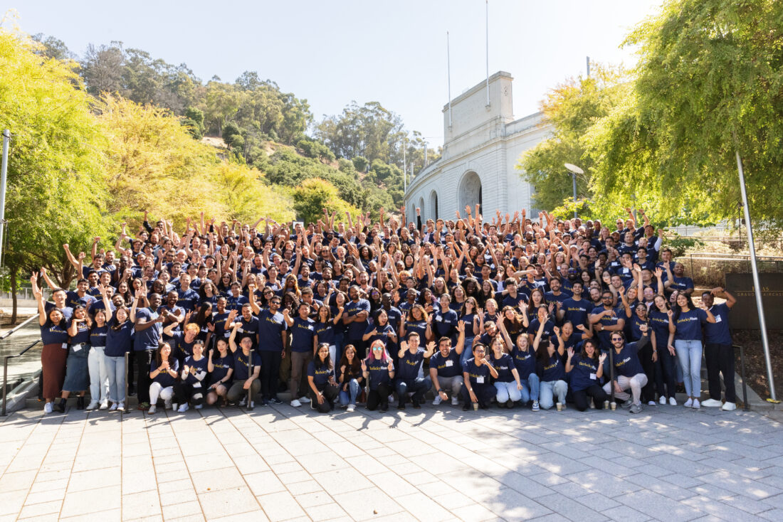 Group portrait of about 300 MBA students posing on steps to the Cal Memorial Stadium. They are wearing Berkeley Haas t-shirts and waving to the camera.