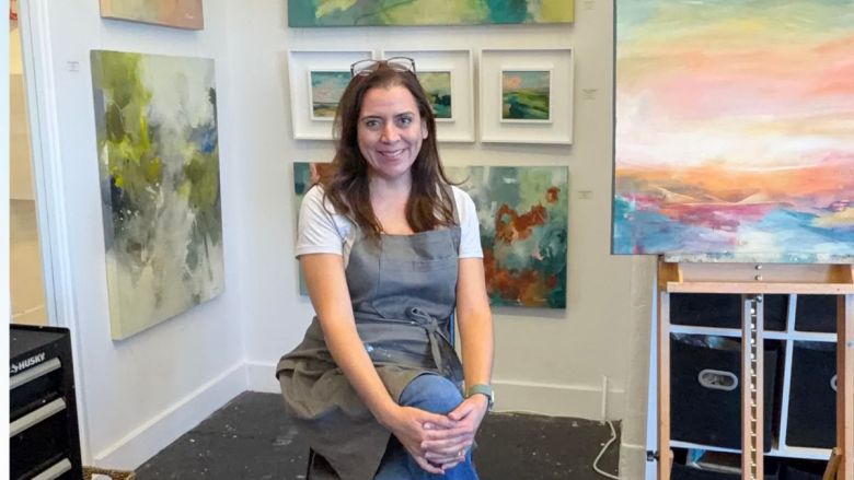A woman in an art studio surrounded by abstract paintings.
